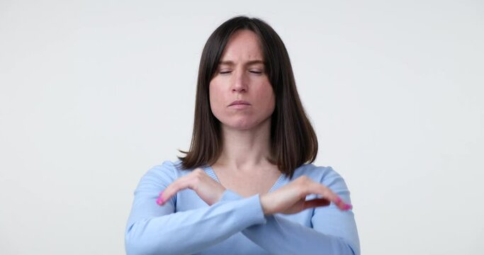 A Caucasian woman stands on a white background and makes a stop gesture in denial, crossing her arms in front of her with a serious expression on her face.