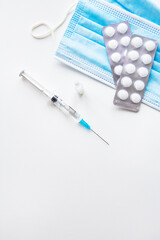 Preparation for vaccination against covid-19. Thermometer, pills, medical mask on a white table. Place for an inscription, vertical photo.