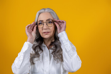 Intelligent senior woman in eyeglasses on yellow background