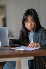 Long-haired young asian girl in eyeglasses looking serious and involved