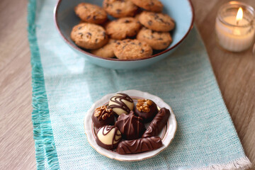 Plate of chocolate pralines, bowl of cookies, cups of tea, glasses of juice and lit candles on the table. Selective focus.