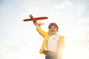 Against cloudy sky. Little boy is playing with toy plane on the summer field