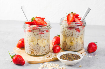 Overnight Oats with Fresh Strawberry, Banana and Chia Seeds in Jars on Light Grey Background, Healthy Snack or Breakfast