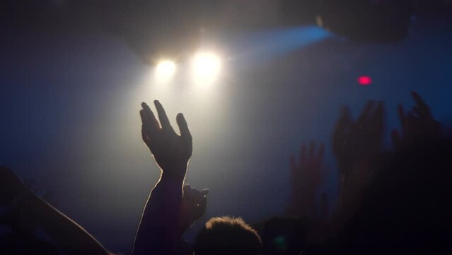 Fans raise their hands in the air during a concert of a musical group on the stage of a nightclub. Back view of a crowd of dancing people in slow motion. High quality 4k footage
