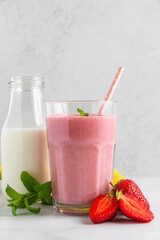 Strawberry and banana milkshake in a glass with a straw, fresh fruits and bottle of milk on white background. Vertical orientation
