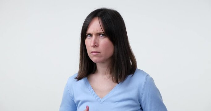 A Caucasian woman stands on a white background and looks directly at the camera. Suddenly, she becomes startled and frightened, showing a reaction of fear.