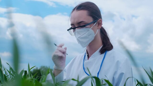 Portrait of a caucasian woman in goggles and a white uniform smiling at the camera, standing on a farm. The laboratory assistant is confident in the benefits of organic greens.