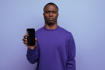 authentic handsome young african man in blue sweater holding smartphone vertically with mockup for advertisement on blue background with copy space