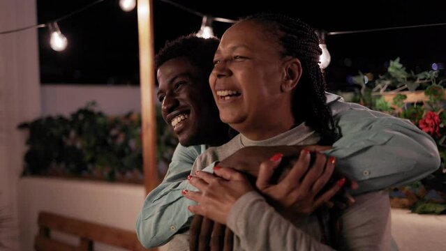 Happy African mother and son having fun hugging each other at night in home patio terrace
