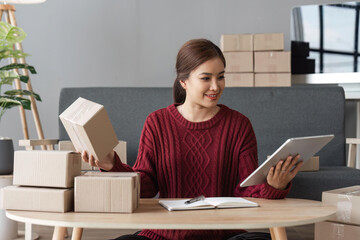 Naklejka premium Asian woman holding parcel boxes and holding laptop, she owns an online store. Online selling concept