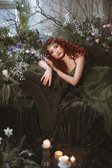 gorgeous woman with red curly hair sits on the sofa decorated with spring flowers and plants, flora...