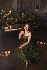 fairy red hair woman sitting on the floor near the grand piano decorated with candles, flowers and...