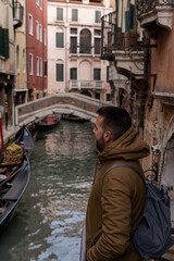 Fototapeta na wymiar Young male tourist looking towards the canals of Venice with gondolas