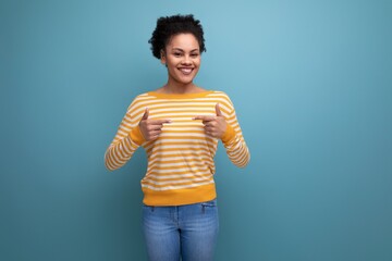 joyful cute brunette curly latin young woman in yellow striped sweater