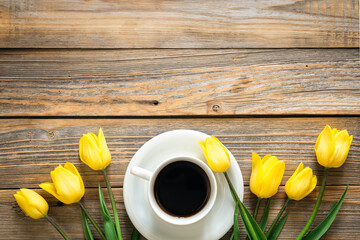 Bouquet of yellow tulips and cup of coffee on a wooden background, top view.
