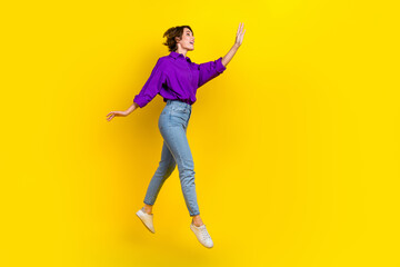 Fototapeta na wymiar Full length photo of dreamy excited woman dressed purple shirt jumping waving arm empty space isolated yellow color background