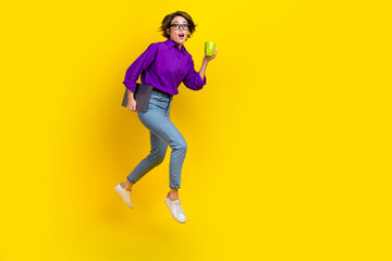 Fototapeta na wymiar Full length photo of impressed woman dressed purple shirt jumping holding gadget drink tea empty space isolated yellow color background