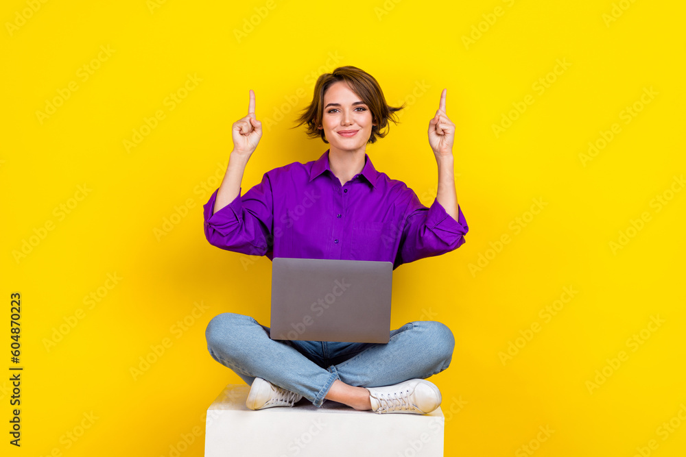 Poster Full size photo of pretty positive girl sit podium direct fingers up empty space use netbook isolated on yellow color background