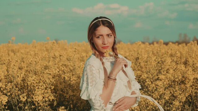 Beautiful young woman in white dress on yellow flower meadow in sunset