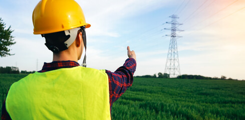 Construction worker pointing to the electricity pylon. Electrician wearing yellow hard hat and...