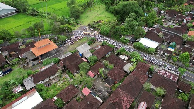 Big procession of people wearing white closes, walking slowly at village street. Aerial perspective of Melis Day parade, group of citizens waiting at road turn to join ceremonial walk to beach.