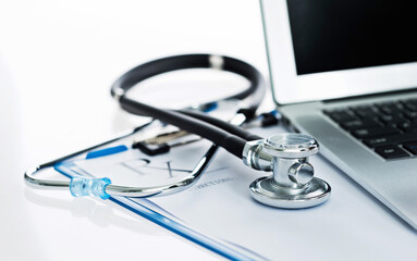 Stethoscope with clipboard and laptop on desk