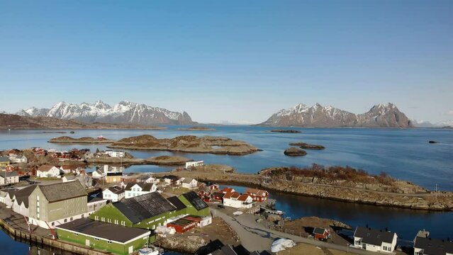 Aerial drone shot of cottages in Lofoten Norway with big mountains in the background. surrounded by the ocean.