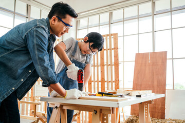 Asian father and son work as a woodworker or carpenters. Close up hands of the father and his son drill holes in a wooden plank carefully together. carpentry working at a home workshop studio.
