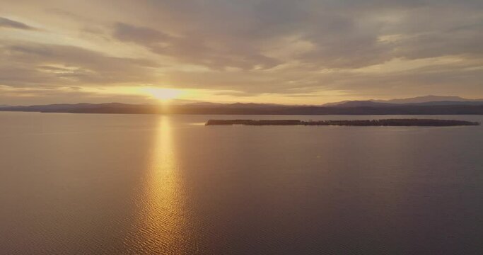 4K drone aerial footage of Sunset with sun rays flaring and reflecting over an island on Lake Champlain in Vermont Adirondack mountains in the background