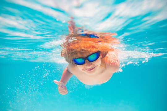 Summer child boy relax at aquapark. Summertime vacation. Little kid swim underwater in pool. Kid wearing summer goggles swims under water in poolside. Underwater photo.