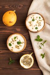 Yoghurt with granadilla and mint in wooden bowl on brown wooden, top view.