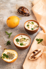 Fototapeta na wymiar Yoghurt with granadilla and mint in clay bowl on brown concrete, side view