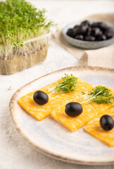 Marble cheese with olives and watercress microgreen on gray concrete. side view, selective focus.