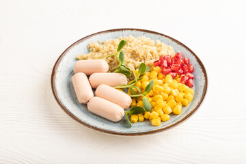 Mixed quinoa porridge, sweet corn and small sausages on white wooden, side view.