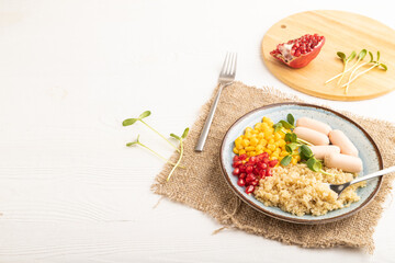 Mixed quinoa porridge, sweet corn and small sausages on white wooden, side view, copy space.