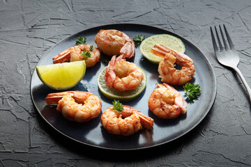 Shrimps. Fried shrimp with lime on a blue plate, on a black slate background. Spicy seafood dinner