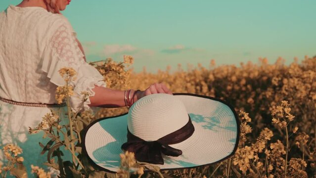 Beautiful young woman in white dress on yellow flower meadow in sunset