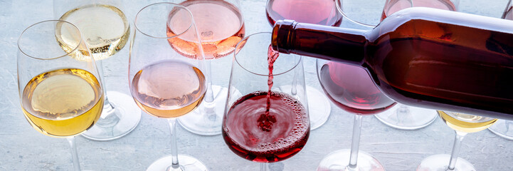 Red wine pour into a glass at a tasting panorama. Rose, red, and white wine, drinks on a table. An assortment of wines of many different colors - 604881496