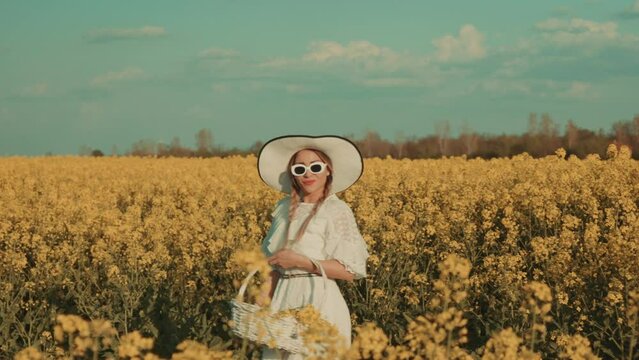 Beautiful young woman in white dress on yellow flower meadow in sunset