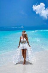 Fototapeta na wymiar Bride on the beach. Stylish female model in elegant long gown dress on the Maldives beach. Elegance. Bride on Maldives. Bridal fashion. Classy woman in amazing ruffle white dress. Luxury travel