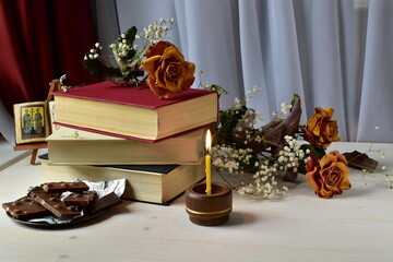 still life with chocolate, a stack of books, dry flowers and a burning candle