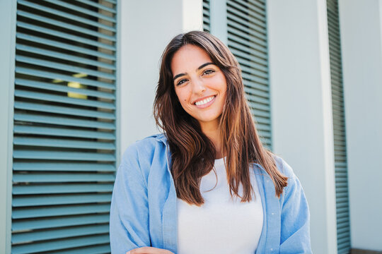 Happy caucasian young student female looking at camera enjoying with a perfect white teeth. Portrait of a joyful and adorable teenage brunette woman posing for a college promotion with crossed arms