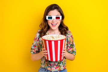 Photo of positive shocked girl hold big pop corn bucket enjoy 3d film in cinema isolated bright...