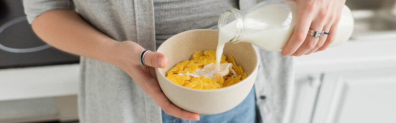 cropped view of tattooed young woman holding bottle while pouring fresh milk into bowl with...