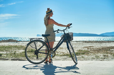 Carefree woman with bike riding on sand beach having fun, on the seaside promenade on a summer day.