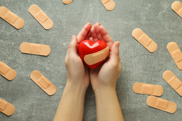 Female hands hold heart on gray background with adhesive plaster