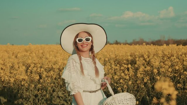 Beautiful young woman in white dress on yellow flower meadow in sunset