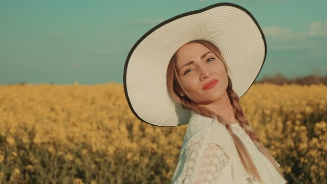 Beautiful young woman in white dress on yellow flower meadow in sunset