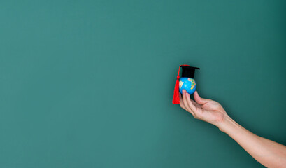 Hand hold a globe and mortarboard in front of blackboard - obrazy, fototapety, plakaty