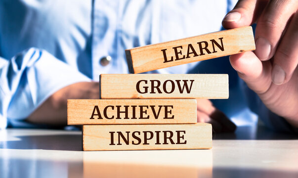 Close up on businessman holding a wooden block with the "Learn, grow, achieve, inspire" message
